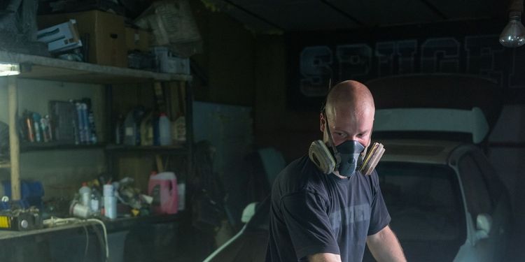 A painter in a respirator spraying a car in a paint booth