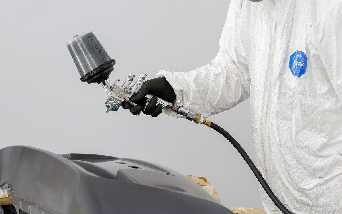 A painter in a white suit spraying a bumper