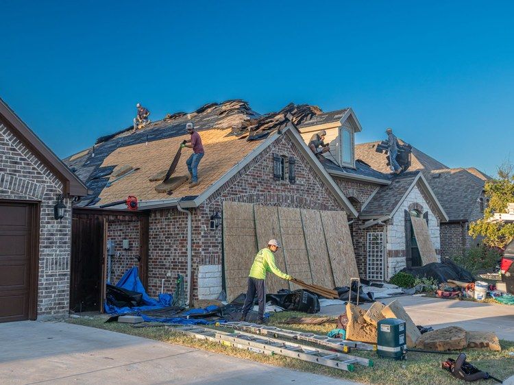 A roofing crew tearing off an old roof on a brick house